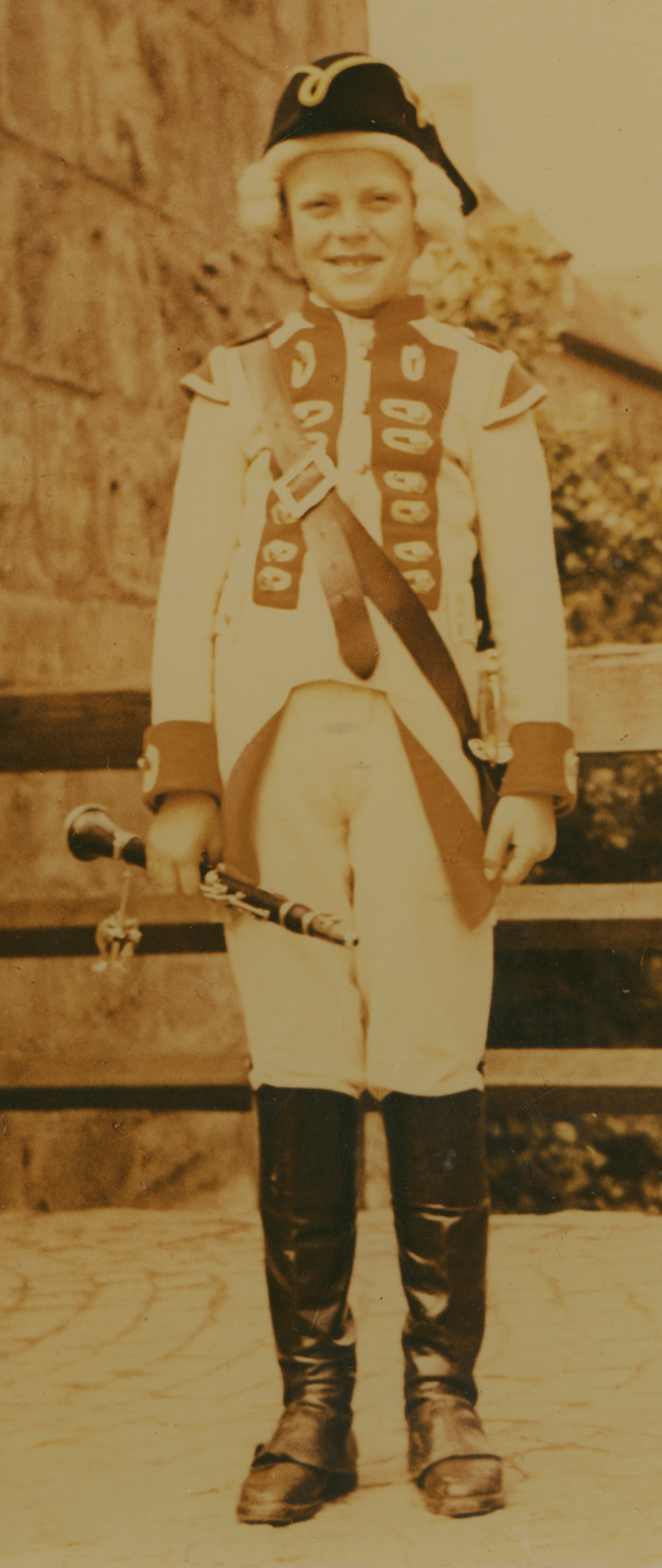 Ein Junge in historischer Uniform hält eine Es-Klarinette in seiner rechten Hand; er steht vor einem Stadttor der Stadt Dinkelsbühl.