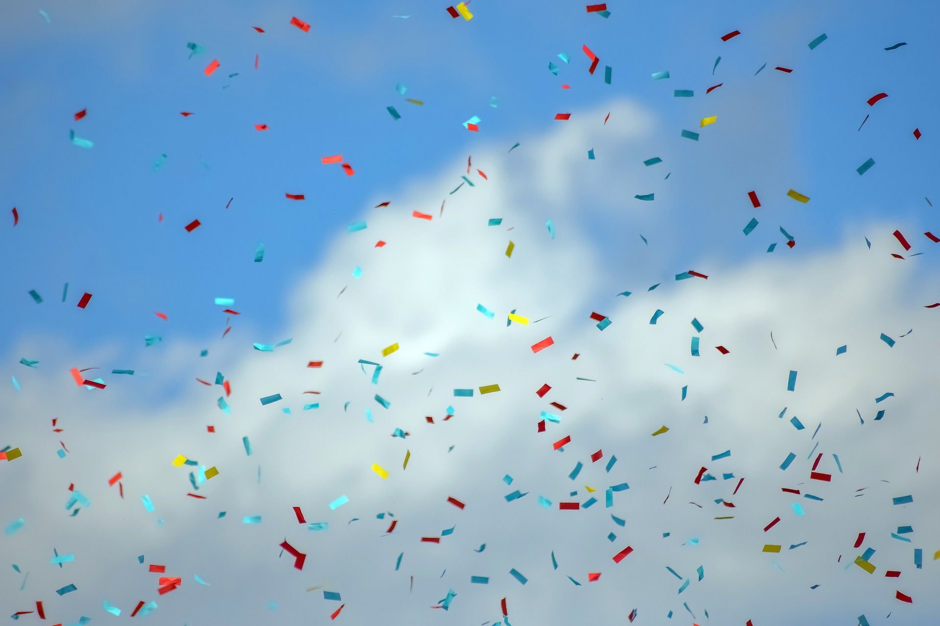 Bunte Konfetti flirren unter blauem Himmel mit weißen Wolken.