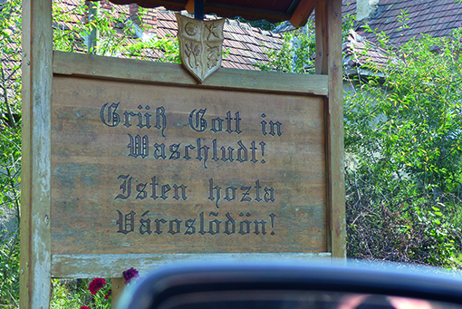 Eine Holztafel begrüßt am Ortseingang die Gäste mit den Worten Grüß Gott in Waschludt! Isten hozta Városlödön!