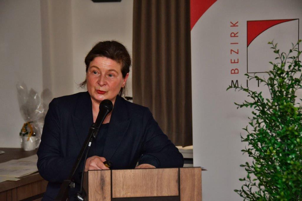 Die stellvertretende Bezirksheimatpflegerin und Kulturreferentin Julia Krieger am Rednerpult bei der Denkmalprämierung 2024. Rechts daneben das Logo des Bezirks Mittelfranken und Blumenschmuck. Foto: Thomas Scherer