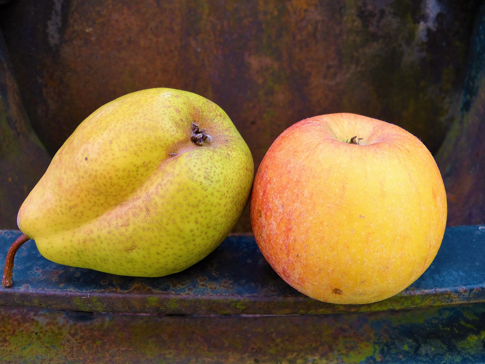 Eine Birne und ein Apfel liegen auf dem Rand eines Metallgefäßes.